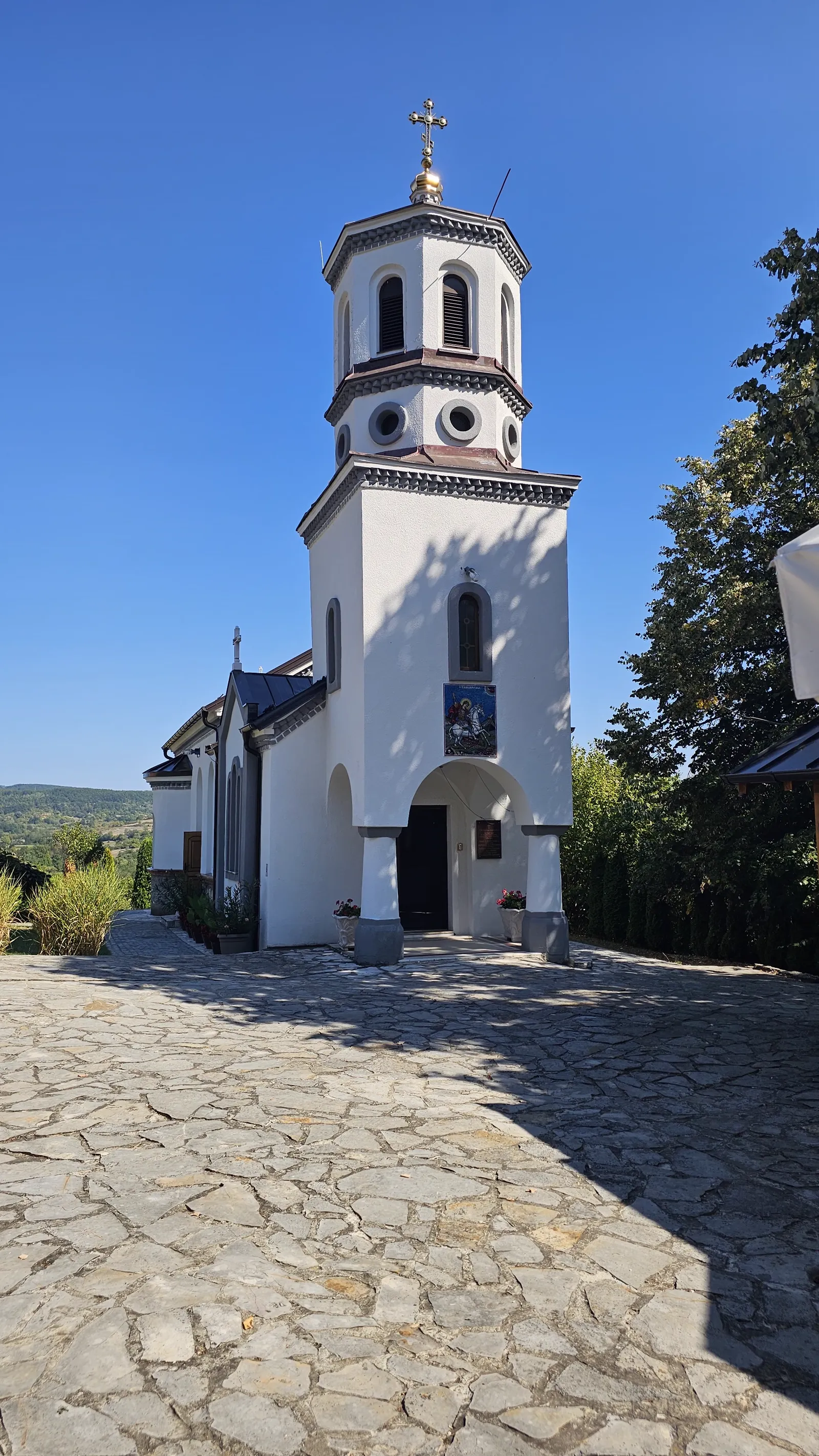 Beli zvonik sa krstom i ulaz u crkvu manastira Lipar pod vedrim nebom